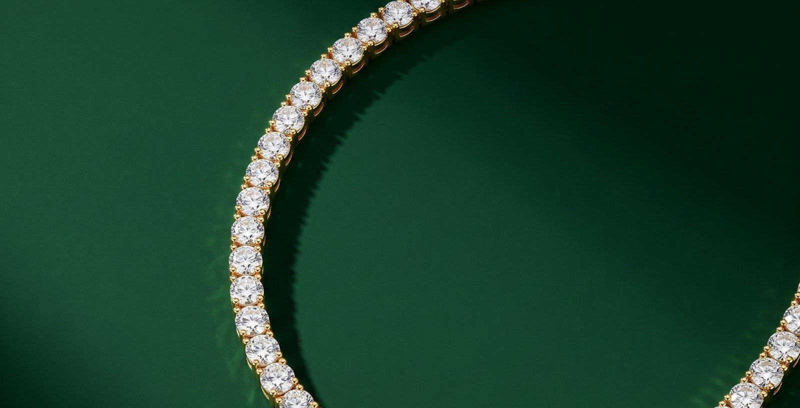 A gold tennis necklace laid in an open curve on a deep green ground